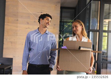 Colleagues smiling while carrying box in modern office, enjoying teamwork 135532826