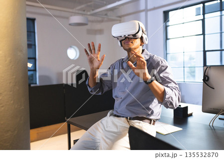 Businessman using VR headset at office, exploring virtual reality with excitement 135532870
