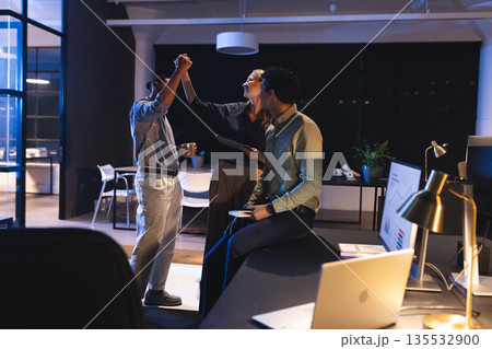 Celebrating success, diverse colleagues high-fiving in modern office at night Celebrating success, diverse colleagues high-fiving in modern office at night 135532900
