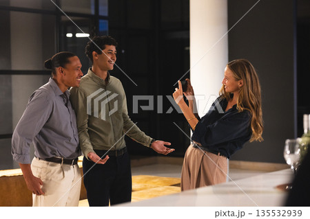 Colleagues enjoying after-work gathering, woman capturing fun moment with smartphone Colleagues enjoying after-work gathering, woman capturing fun moment with smartphone 135532939