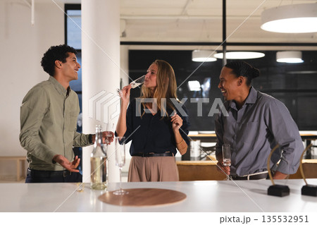 At office gathering, colleagues drinking and laughing, enjoying evening together At office gathering, colleagues drinking and laughing, enjoying evening together 135532951