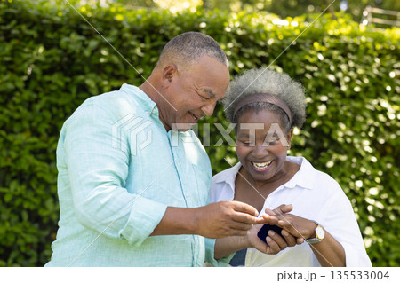 Exchanging rings and smiling, African American senior couple celebrating love in garden Exchanging rings and smiling, African American senior couple celebrating love in garden 135533004