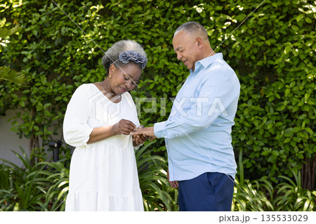 Senior couple exchanging rings in garden, sharing joyful moment together Senior couple exchanging rings in garden, sharing joyful moment together 135533029