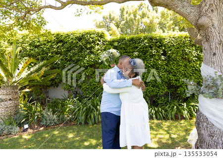 Senior couple embracing under tree in garden, enjoying peaceful moment together 135533054
