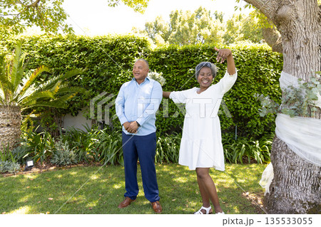 Senior couple enjoying sunny day in garden, woman dancing joyfully beside partner Senior couple enjoying sunny day in garden, woman dancing joyfully beside partner 135533055