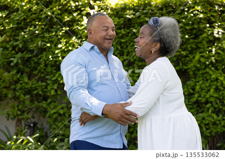 Senior couple laughing and embracing outdoors in lush green garden Senior couple laughing and embracing outdoors in lush green garden 135533062