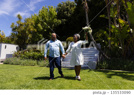 African American couple walking hand in hand in garden, woman holding flowers 135533090