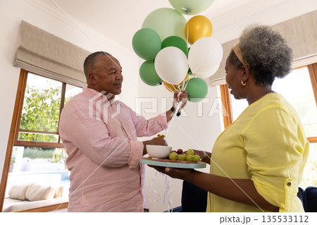 Senior couple enjoying balloons and fruit platter at home, sharing joyful moment Senior couple enjoying balloons and fruit platter at home, sharing joyful moment 135533112