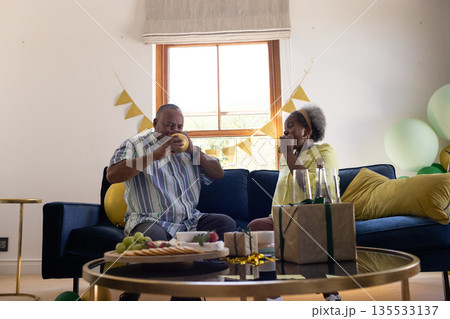 African American senior couple enjoying snacks and drinks at home celebration 135533137