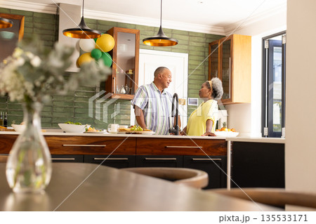 Senior couple enjoying conversation in modern kitchen with festive balloons 135533171