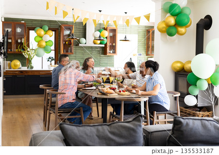 Senior friends celebrating together at home, raising glasses around festive table 135533187