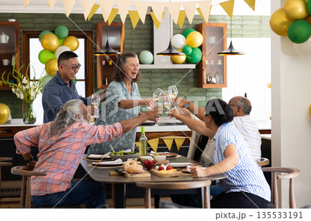 Senior friends celebrating together at home, raising glasses in joyful toast Senior friends celebrating together at home, raising glasses in joyful toast 135533191