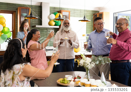 Senior friends celebrating together at home, raising glasses and smiling joyfully 135533201