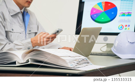 オフィスでPCとスマホを使って仕事する男性作業員 135533315