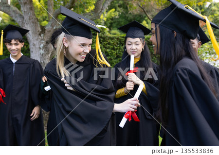 Graduating students in caps and gowns celebrating with diplomas outdoors 135533836