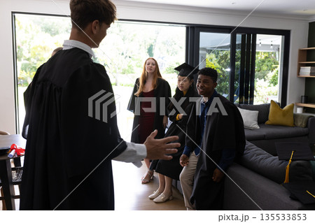 Graduating students in caps and gowns celebrating together at home Graduating students in caps and gowns celebrating together at home 135533853