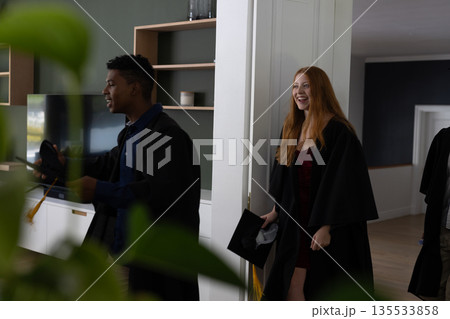 Teens in graduation gowns celebrating and smiling joyfully at home 135533858