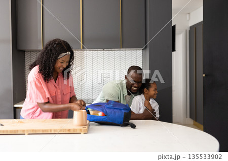In kitchen, parents packing lunch while hugging child, sharing family moment In kitchen, parents packing lunch while hugging child, sharing family moment 135533902