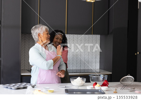 Baking in kitchen, African American woman and elderly woman sharing laughter together Baking in kitchen, African American woman and elderly woman sharing laughter together 135533928