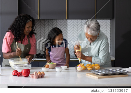 Three generations baking cupcakes together in modern kitchen, sharing joyful moments 135533957