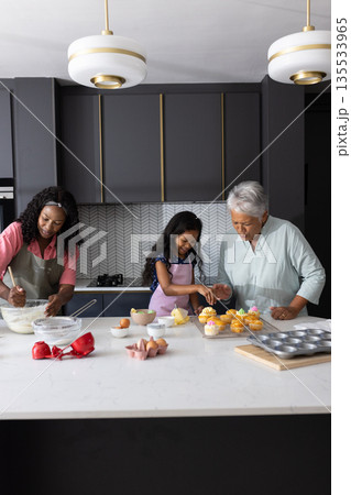 Three generations baking cupcakes together in modern kitchen, enjoying family time Three generations baking cupcakes together in modern kitchen, enjoying family time 135533965