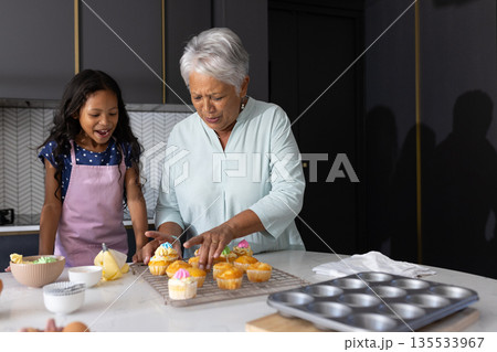 Decorating cupcakes, grandmother and child in modern kitchen, spending time together 135533967