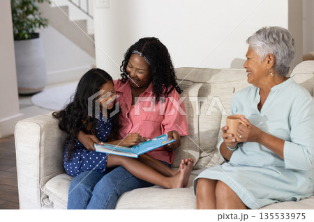 Reading book on couch, African American mother and child with smiling grandmother Reading book on couch, African American mother and child with smiling grandmother 135533975
