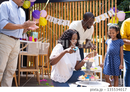 Celebrating birthday outdoors, family decorating cupcakes with colorful candles and balloons 135534017