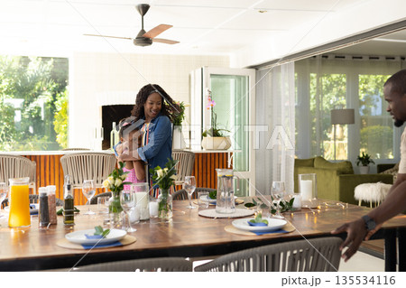 African American mother hugging daughter while father sets dining table at home African American mother hugging daughter while father sets dining table at home 135534116