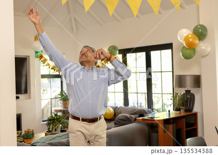 Middle-aged man adjusting yellow pennant banner in living room, with green balloons Middle-aged man adjusting yellow pennant banner in living room, with green balloons 135534388