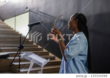 African American woman holding award plaque and speaking at podium in auditorium, copy space 135534399