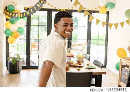 Diverse young man smiling, reaching to hold hand in dining room with birthday cake and balloons 135534412