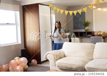 Woman arranging plates in living room with bunting, balloons and string lights for celebration 135534416