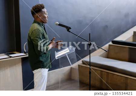 African American man speaking at lectern in lecture hall, with microphone and papers, copy space 135534421