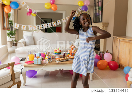 African American child girl dancing in living room, celebrating with cake and balloons, copy space 135534453