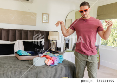 Young adult woman packing colorful clothes into open suitcase on bed in modern bedroom, copy space 135534455