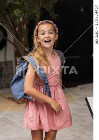 girl turning toward camera on paved patio, wearing pink headband and carrying denim backpack 135534457