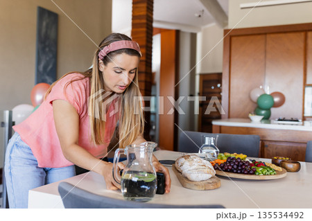 Woman photographing cutting board with bread and grapes using smartphone in kitchen, copy space Woman photographing cutting board with bread and grapes using smartphone in kitchen, copy space 135534492