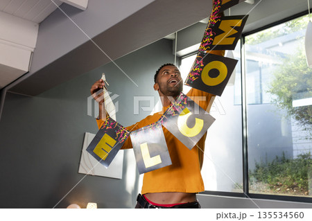 African American man moving WELCOME banner under slanted beam in living room with canvas and lamp 135534560