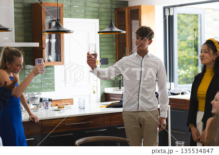 Teen friends celebrating at home, raising glasses and smiling in kitchen Teen friends celebrating at home, raising glasses and smiling in kitchen 135534847