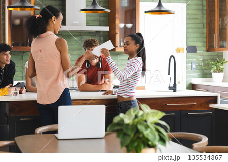 Teen girl receiving card from woman in kitchen, friends smiling in background 135534867