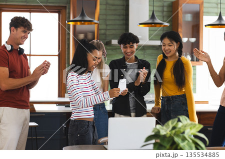 Teen friends celebrating together at home, smiling and clapping around laptop Teen friends celebrating together at home, smiling and clapping around laptop 135534885