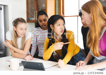 Teenagers collaborating on school project, discussing ideas around tablet at home 135534946