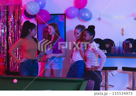 Teen girls enjoying party together, chatting and laughing near pool table Teen girls enjoying party together, chatting and laughing near pool table 135534973