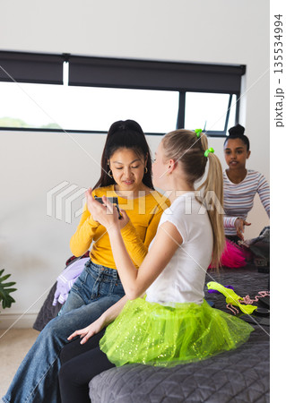 Teen girls enjoying smartphone together while preparing for celebration at home Teen girls enjoying smartphone together while preparing for celebration at home 135534994