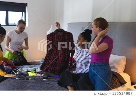Teen girls choosing outfits together on bed, preparing for school event Teen girls choosing outfits together on bed, preparing for school event 135534997