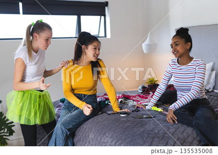 Teen girls chatting and laughing while planning outfits in cozy bedroom Teen girls chatting and laughing while planning outfits in cozy bedroom 135535008