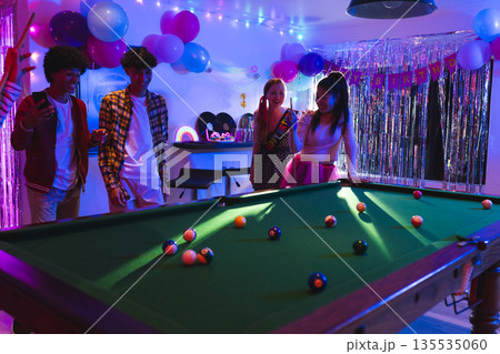Teens enjoying birthday party playing pool in festive, colorful room with balloons Teens enjoying birthday party playing pool in festive, colorful room with balloons 135535060