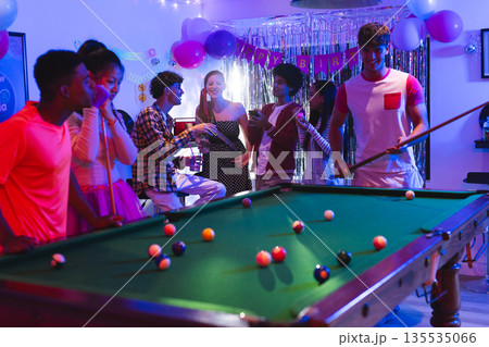Teenagers enjoying lively birthday party playing pool in festive decorated room Teenagers enjoying lively birthday party playing pool in festive decorated room 135535066