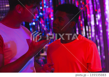 Teenagers in colorful lights at vibrant party, engaging in lively conversation 135535083